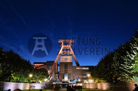 Die Geschichte Zollvereins beginnt in den Pioniertagen des heutigen Ruhrgebiets. Der erste Schacht wurde 1847 abgeteuft, vier Jahre später die erste Kohle gefördert: Vier weitere Anlagen entstanden, die letzte war die Schachtanlage Zollverein XII,  die ab 1932 die Förderung der gesamten Zollverein-Kohle zentral übernahm. 

Die Gebäude der 1928 bis 1932 im Stil der „Neuen Sachlichkeit“ nach Entwürfen der Architekten Fritz Schupp und Martin Kremmer gebauten Anlage sind nach dem Prinzip „Form follows Function“ zum optimalen Ablauf der Kohleförderung und -aufbereitung angeordnet. Trotz Rekordzahlen wie 12.000 Tagestonnen verwertbarer Steinkohle machte das Ende der Schwerindustrie auch vor Zollverein nicht Halt. Am 23. Dezember 1986 fuhr die letzte Schicht ein. An diesem Tag stand die Zeche bereits unter Denkmalschutz, 1990 begannen die Sanierungsarbeiten und seit 2001 sind Zeche und Kokerei Zollverein UNESCO-Welterbe. Mit dem Denkmalpfad ZOLLVEREIN®, dem Ruhr Museum und dem Red Dot Design Museum sind auf Schacht XII drei der beliebtesten Touristenziele der Region angesiedelt. Das Doppelbock-Fördergerüst der Schachtanlage ist heute ein Wahrzeichen für das gesamte Ruhrgebiet. 

Das 55 Meter hohe Doppelbock-Fördergerüst ist das Wahrzeichen der Zeche Zollverein, der Stadt Essen und der gesamten Region: Die als Doppelstrebengerüst in Vollwandbauweise konstruierte Förderanlage ermöglichte eine doppelte Fördermechanik, mittels derer die doppelte Menge Förderwagen bzw. Fördergefäße transportiert werden konnten. Zollverein Schacht XII galt zu Betriebszeiten als die leistungsstärkste Zeche der Welt. 250 Stufen führen auf die oberste Plattform des Gerüstes, deren Seilscheiben sich auch heute noch drehen: Der Schacht wird heute von der RAG AG für die zentrale Wasserhaltung genutzt.

Areal A [Schacht XII], Fördergerüst [A1]