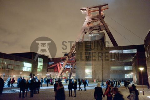 Die Geschichte Zollvereins beginnt in den Pioniertagen des heutigen Ruhrgebiets. Der erste Schacht wurde 1847 abgeteuft, vier Jahre später die erste Kohle gefördert: Vier weitere Anlagen entstanden, die letzte war die Schachtanlage Zollverein XII,  die ab 1932 die Förderung der gesamten Zollverein-Kohle zentral übernahm. 

Die Gebäude der 1928 bis 1932 im Stil der „Neuen Sachlichkeit“ nach Entwürfen der Architekten Fritz Schupp und Martin Kremmer gebauten Anlage sind nach dem Prinzip „Form follows Function“ zum optimalen Ablauf der Kohleförderung und -aufbereitung angeordnet. Trotz Rekordzahlen wie 12.000 Tagestonnen verwertbarer Steinkohle machte das Ende der Schwerindustrie auch vor Zollverein nicht Halt. Am 23. Dezember 1986 fuhr die letzte Schicht ein. An diesem Tag stand die Zeche bereits unter Denkmalschutz, 1990 begannen die Sanierungsarbeiten und seit 2001 sind Zeche und Kokerei Zollverein UNESCO-Welterbe. Mit dem Denkmalpfad ZOLLVEREIN®, dem Ruhr Museum und dem Red Dot Design Museum sind auf Schacht XII drei der beliebtesten Touristenziele der Region angesiedelt. Das Doppelbock-Fördergerüst der Schachtanlage ist heute ein Wahrzeichen für das gesamte Ruhrgebiet. 

Das 55 Meter hohe Doppelbock-Fördergerüst ist das Wahrzeichen der Zeche Zollverein, der Stadt Essen und der gesamten Region: Die als Doppelstrebengerüst in Vollwandbauweise konstruierte Förderanlage ermöglichte eine doppelte Fördermechanik, mittels derer die doppelte Menge Förderwagen bzw. Fördergefäße transportiert werden konnten. Zollverein Schacht XII galt zu Betriebszeiten als die leistungsstärkste Zeche der Welt. 250 Stufen führen auf die oberste Plattform des Gerüstes, deren Seilscheiben sich auch heute noch drehen: Der Schacht wird heute von der RAG AG für die zentrale Wasserhaltung genutzt.

Areal A [Schacht XII], Fördergerüst [A1]